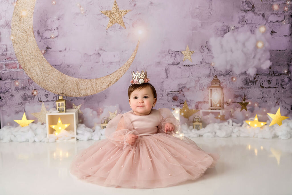Portrait Photographers CT create enchanting first birthday photos of baby girl in blush sparkle tulle gown with golden crown against dreamy moon and stars backdrop