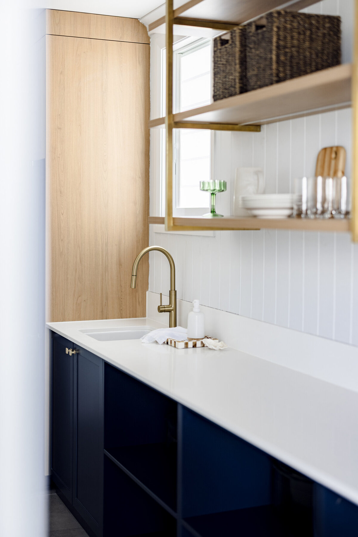 Modern kitchen with navy lower cabinets, white countertop, brass faucet, open shelves, and wooden accents by a bespoke interior design studio in Newcastle NSW.