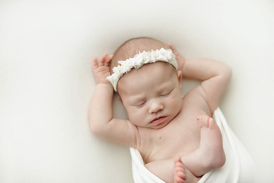 Baby sleeps with hands over head.