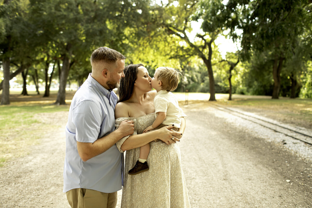 A romantic maternity photo of mom and dad standing in the park, with mom gently cradling her belly while dad wraps his arm around her, captured by Chunky Monkey Photography.