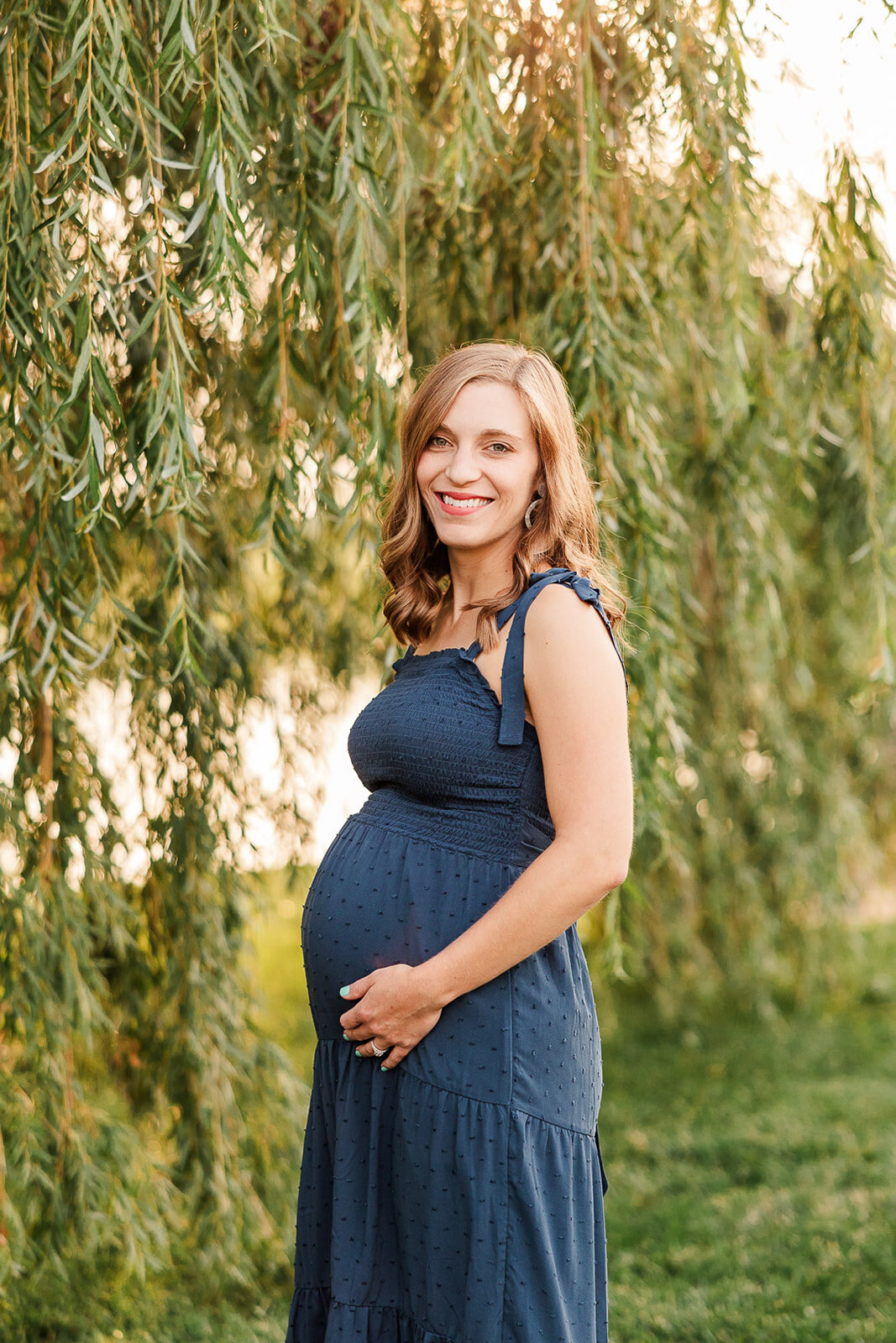 Pregnant woman smiling next to a willow tree