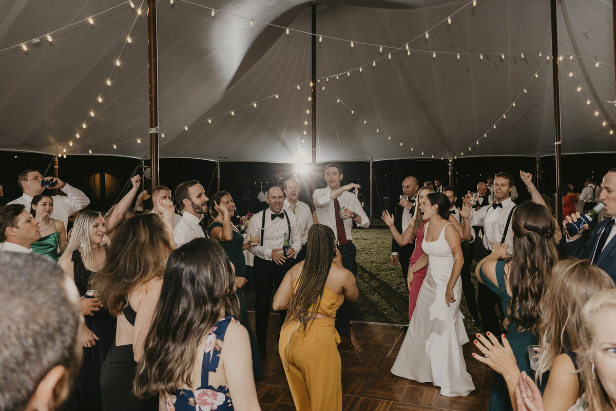 Wedding reception guests dancing under twinkly lights in a tent