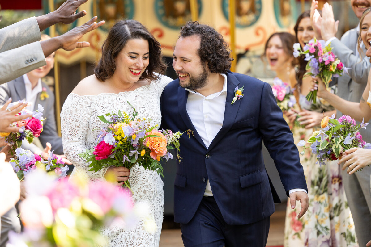 A bride and groom smiling and walking through a tunnel of their wedding parties