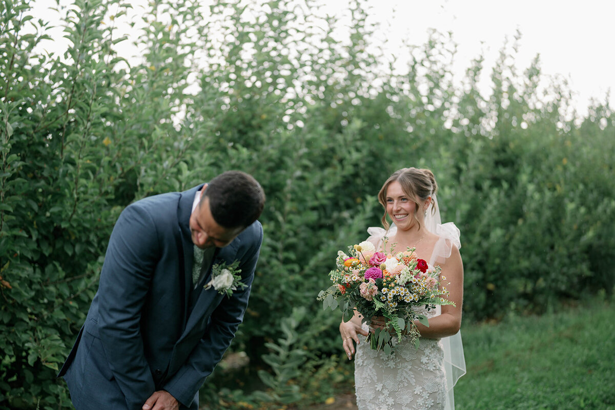Groom tearing up during the emotional first look as he sees his bride in her dress for the first time, with the bride smiling at him during their fall orchard wedding in Frankfort, Michigan.