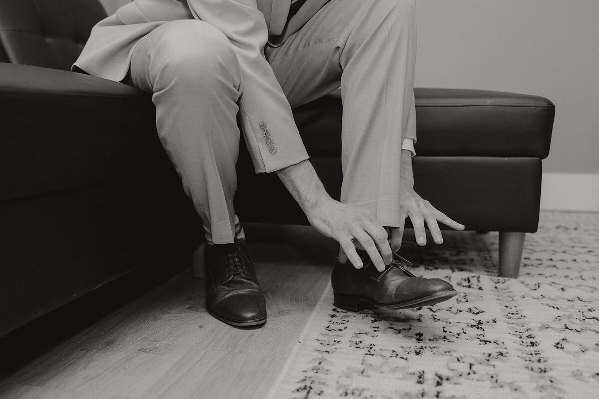 a black and white image of a groom tying his shoes in the Willowbrook wedding venue preparation cottage getting ready suite