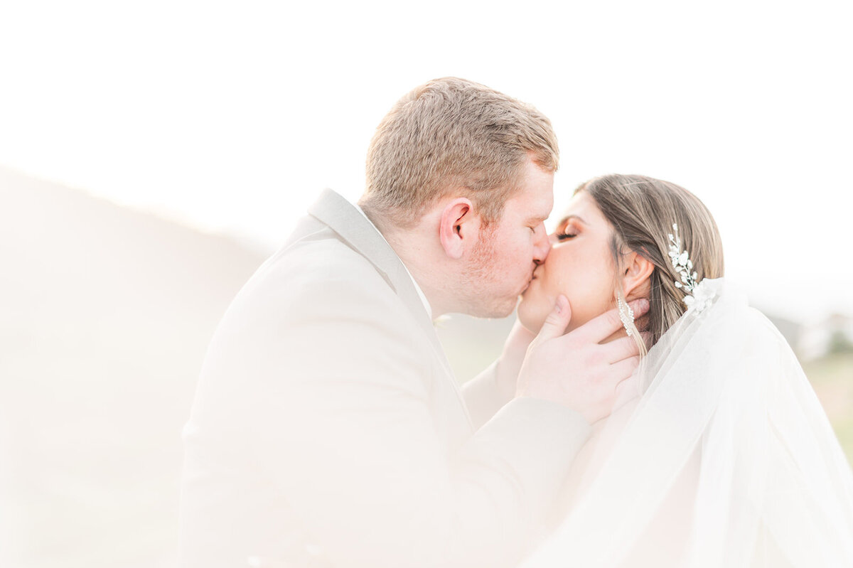 bide and groom kissing at sunset with the veil romantically flowing