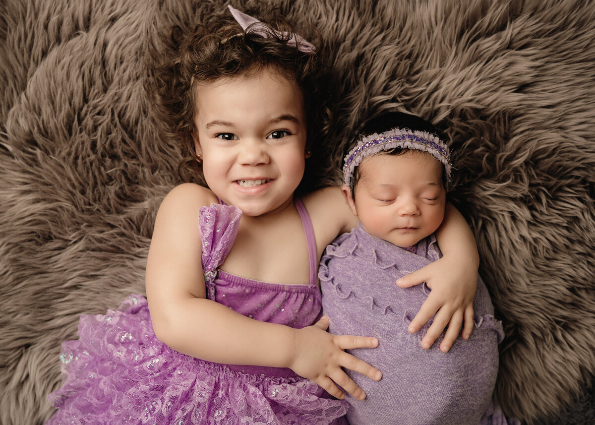 Toddler girl and her sister hugging at studio portrait photo shoot.
