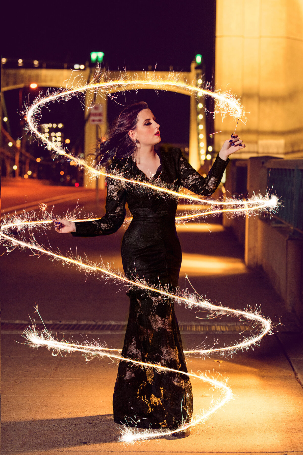 senior photo of girl in black lace dress on bridge at night with sparklers