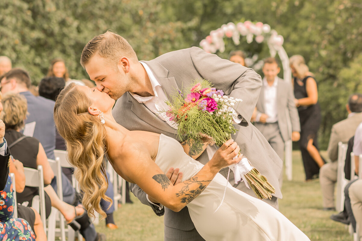 Bride and groom portrait on wedding day after ceremony doing a dip pose as they walk down the aisle