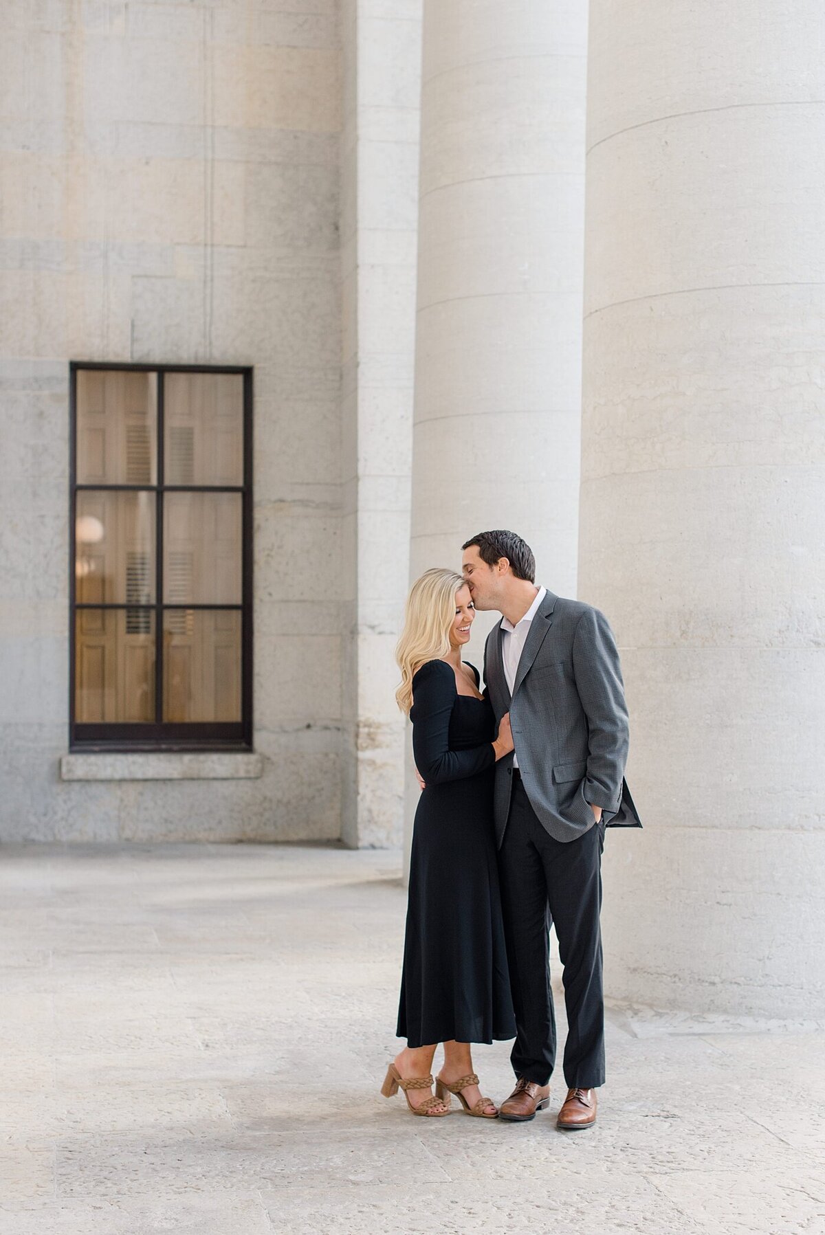 Groom kissing bride by columns at Ohio State House engagement session taken by Ohio Wedding Photographer