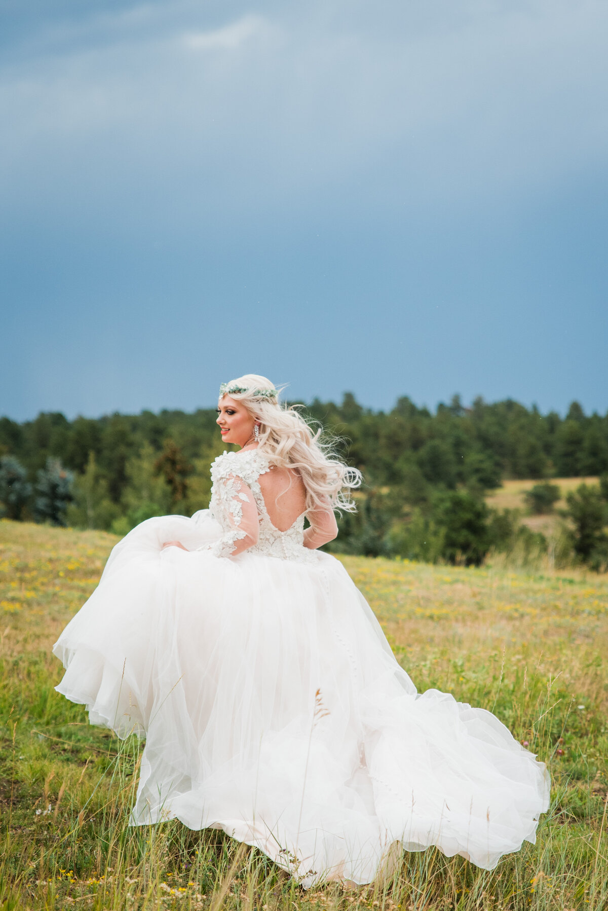 A bride runs away from the camera through a field as she holds the skirt of her dress and her hair blows in the wind.