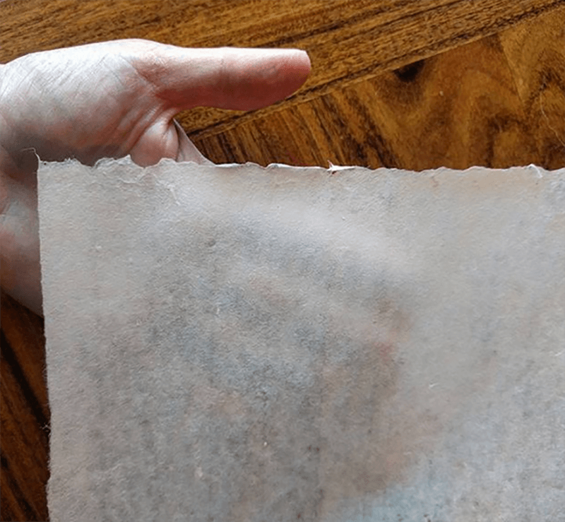 Hand holding a translucent sheet of handmade washi paper, highlighting its fibrous texture.