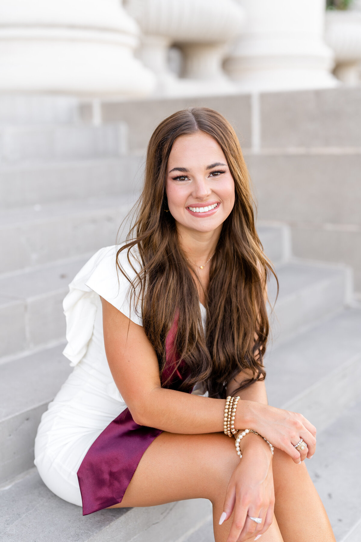 Texas A&M senior girl leaning on legs while sitting on steps of Administration Building while wearing white dress and Aggie stole