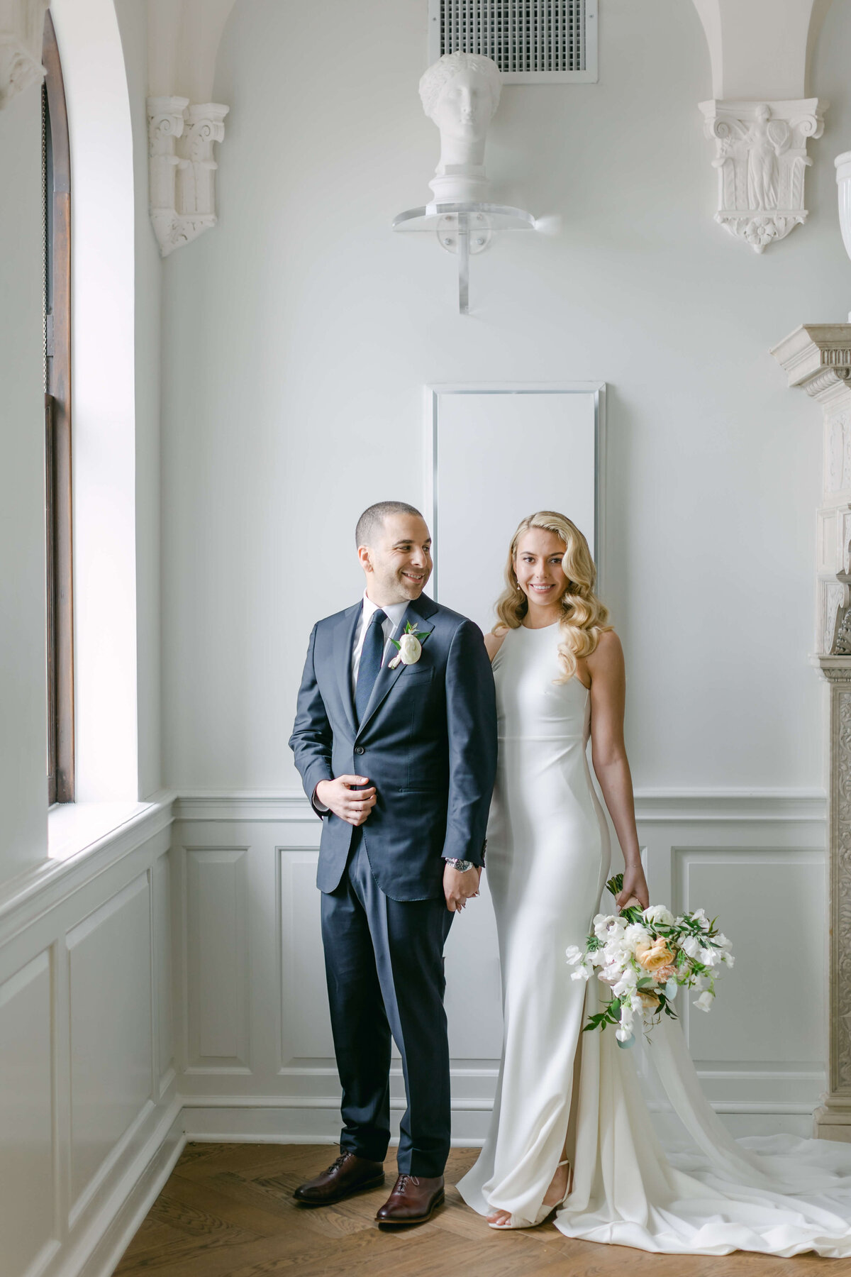 A bride and groom stand in a hallway.