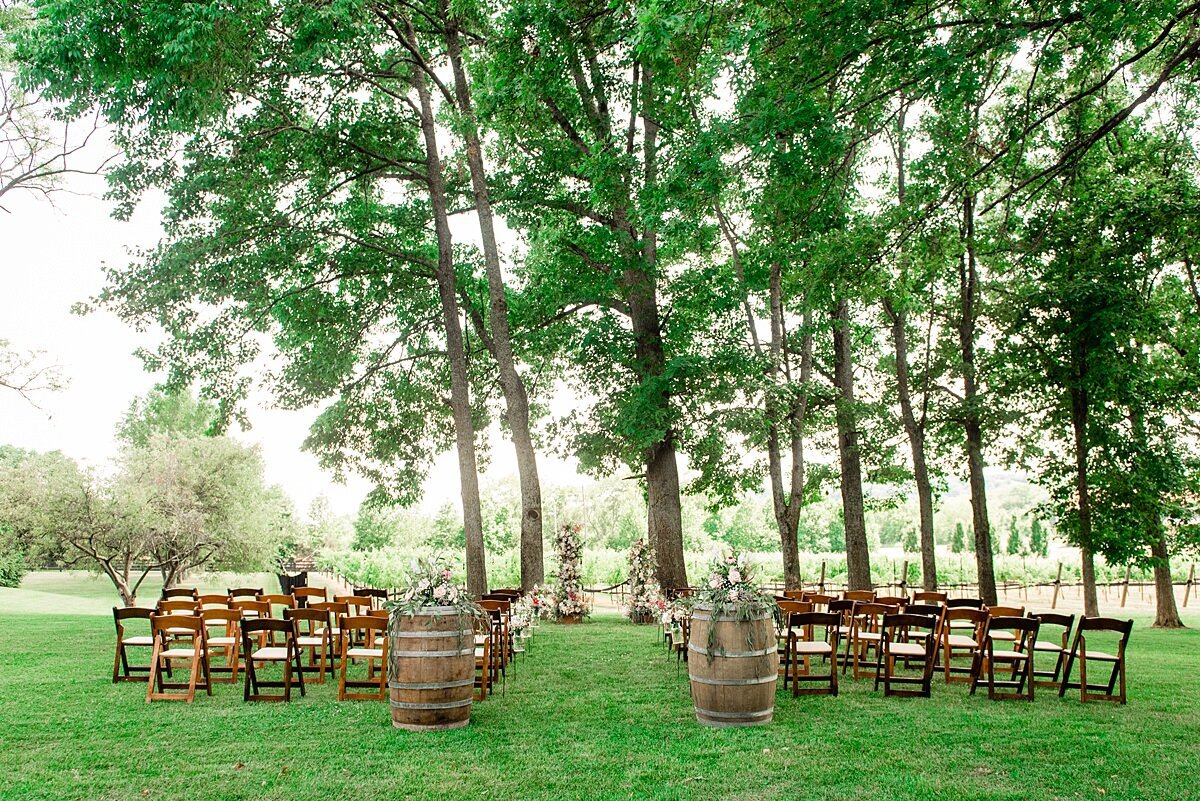 wedding ceremony set outside in a vineyard with wooden garden chairs and two wine barrels as aisle markers
