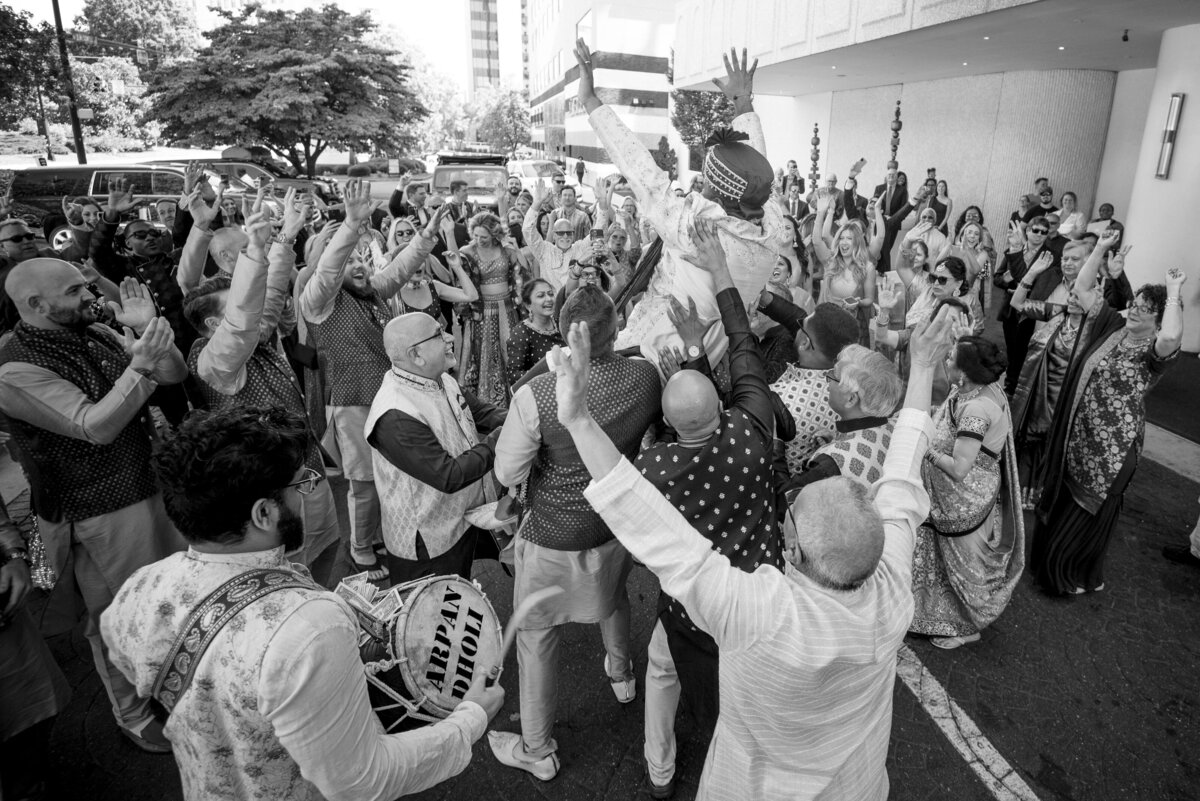 Energetic Indian wedding baraat celebration at Le Méridien Charlotte. The groom is lifted by family and friends while guests dance joyfully to live dhol music. Captured by a Charlotte Indian wedding photographer specializing in vibrant and candid wedding moments.