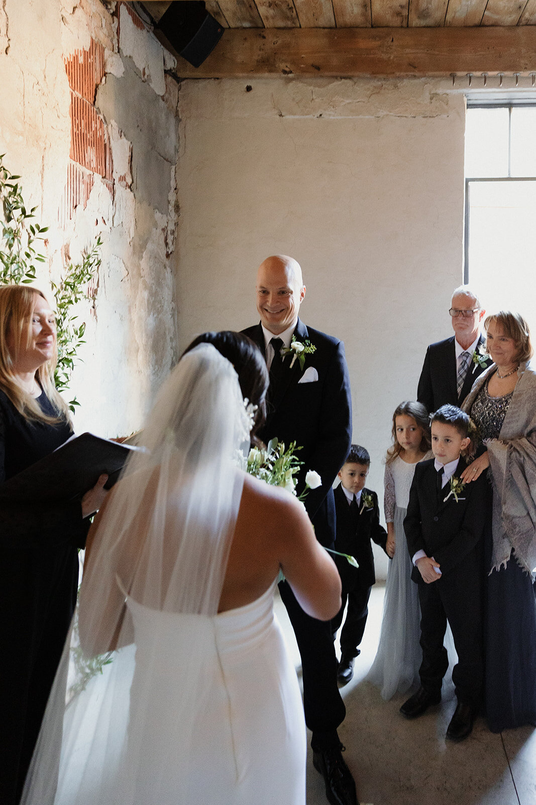 during the ceremony with groom looking at bride and his family behind him