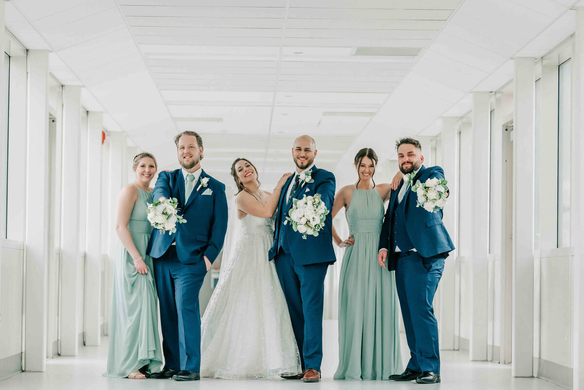 Bride and bridesmaid stand witht he guys. The guys are holding the flowers. 