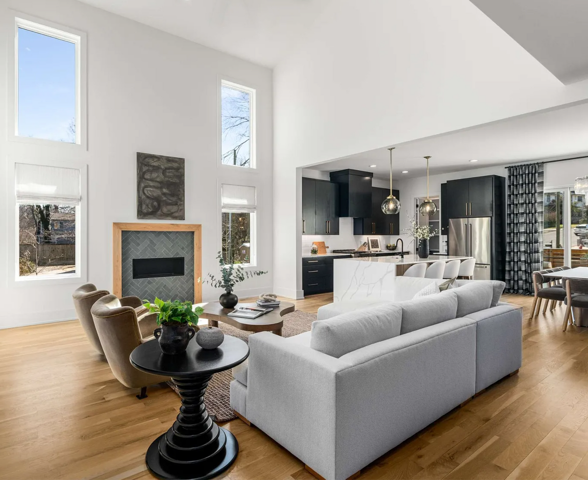 Open-concept living room with high ceilings, modern fireplace, white sectional, black and brass kitchen, quartz waterfall island, and large dining area