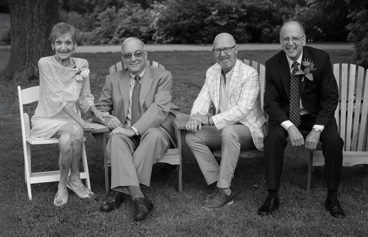 Family poses for portrait during wedding reception while sitting in Adirondack chairs.