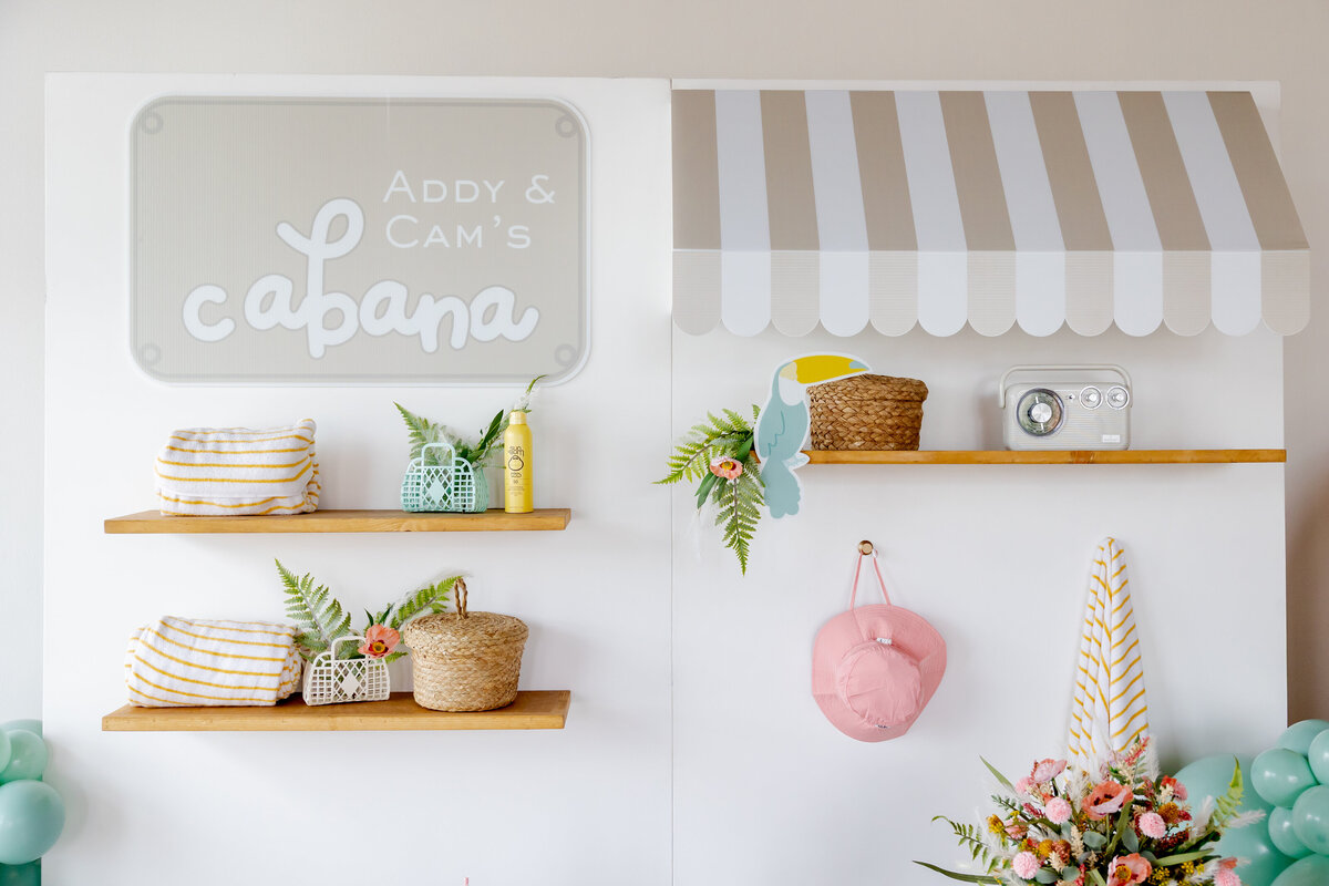 Decorated pool shelves on large wall with baskets, kids hat, sunscreen, flowers and towels. 