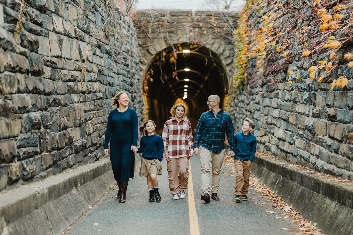 A family of five walks hand in hand surrounded by old stone walls.