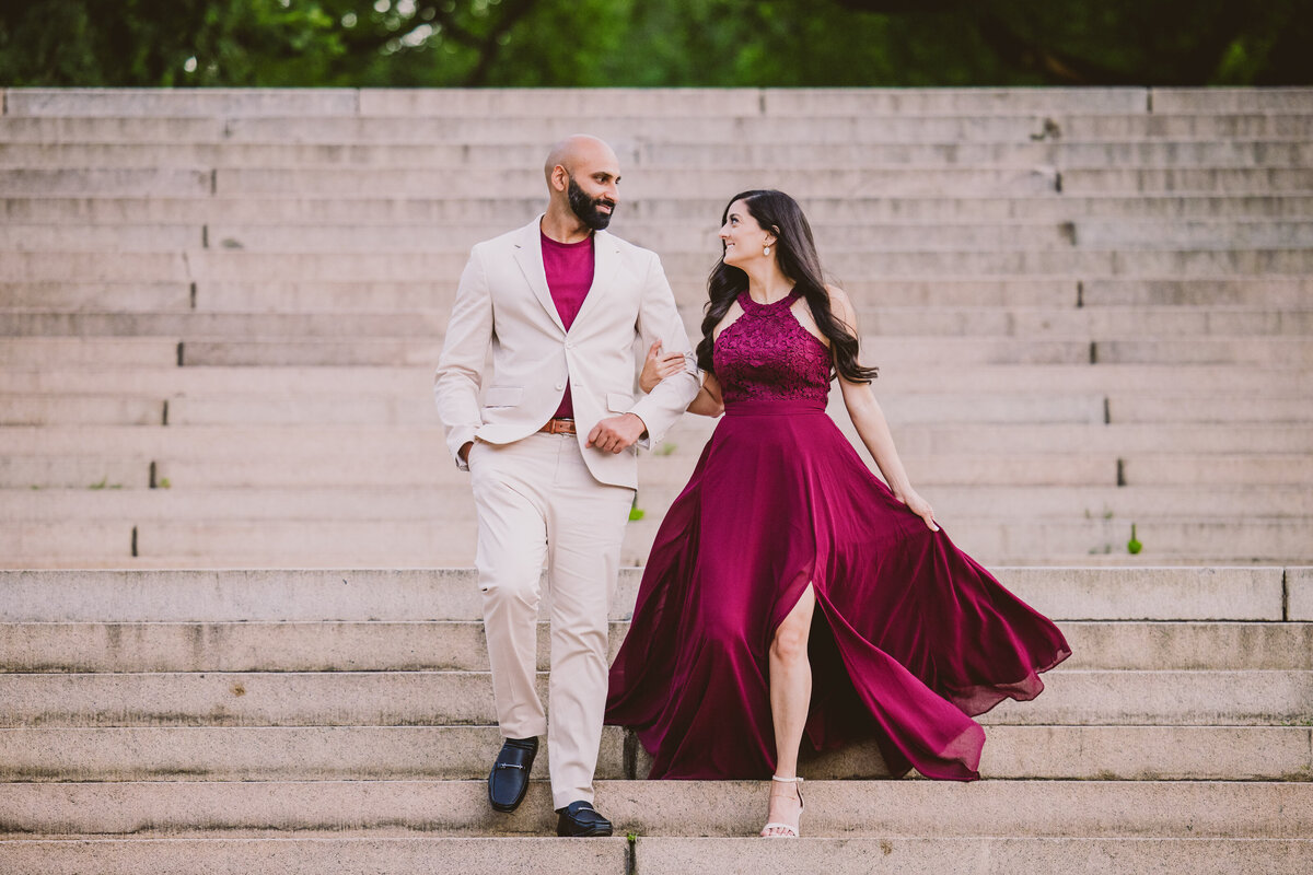 Engaged couple in red outfits walking down the stairs at bethesda terrace in central park