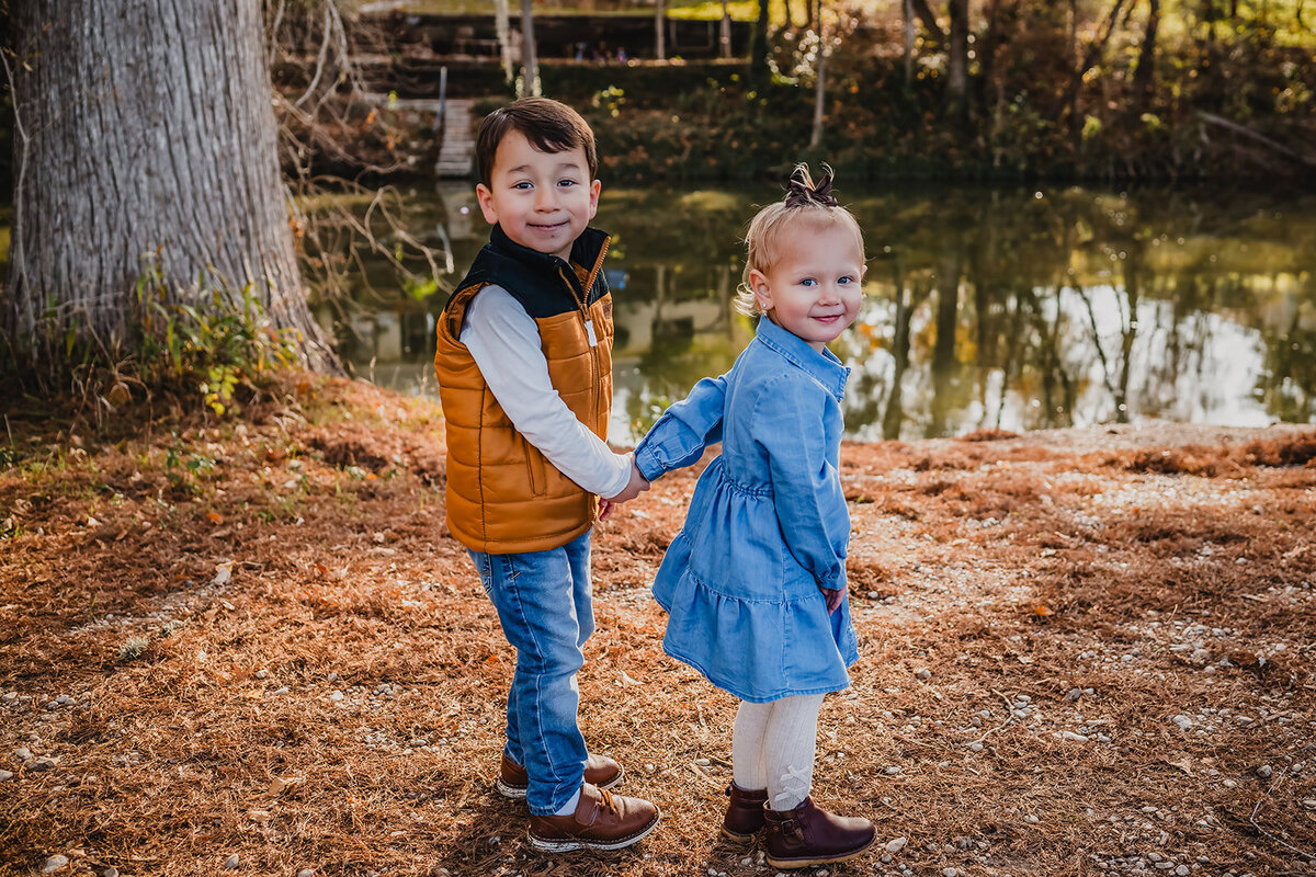 Cousins holding hands and adventuring through field during family session at Cypress Bend in New Braunfels, Texas.