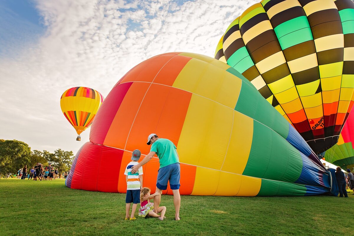 A father and his two children stand in front of a hot air balloon that is being inflated.