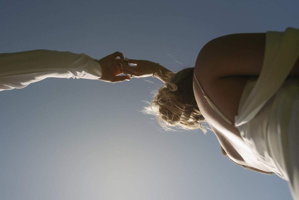 A groom twirling around his bride with the golden hour blue sky above them.