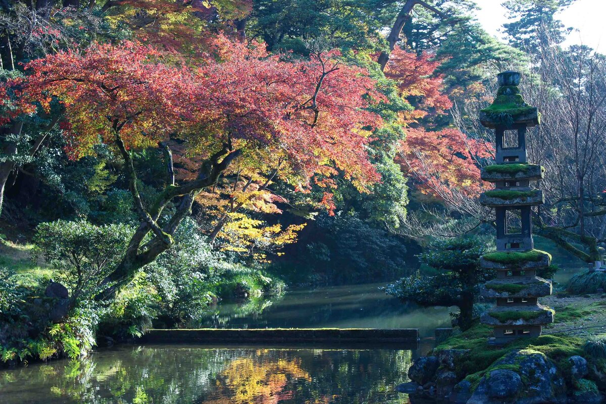 Vibrant autumn foliage reflecting in a tranquil pond beside a moss-covered stone pagoda at Kenroku-en Garden in Ishikawa, Japan ©Stephanie Dosch | theViatrix Luxury Travel