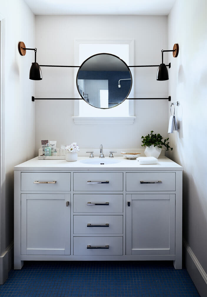 Hingham interior designers design a kid-friendly bathroom with an affordable vanity, bold blue flooring, and a movable mirror covering a small window in a historic home remodel.