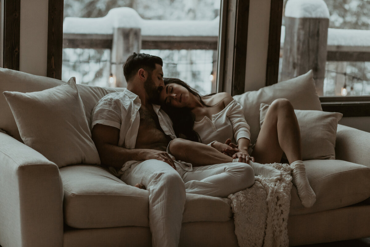 A couple snuggled up on the couch in Kalispell, Montana for an in-home intimate session surrounded by snow and a fireplace
