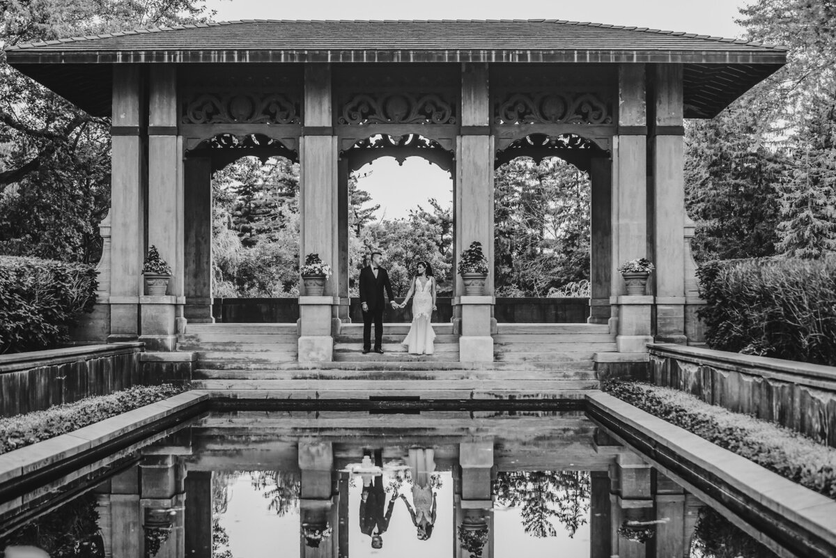 Bride and groom are reflected  in water wt Armour House in Lake Forest, Illinois