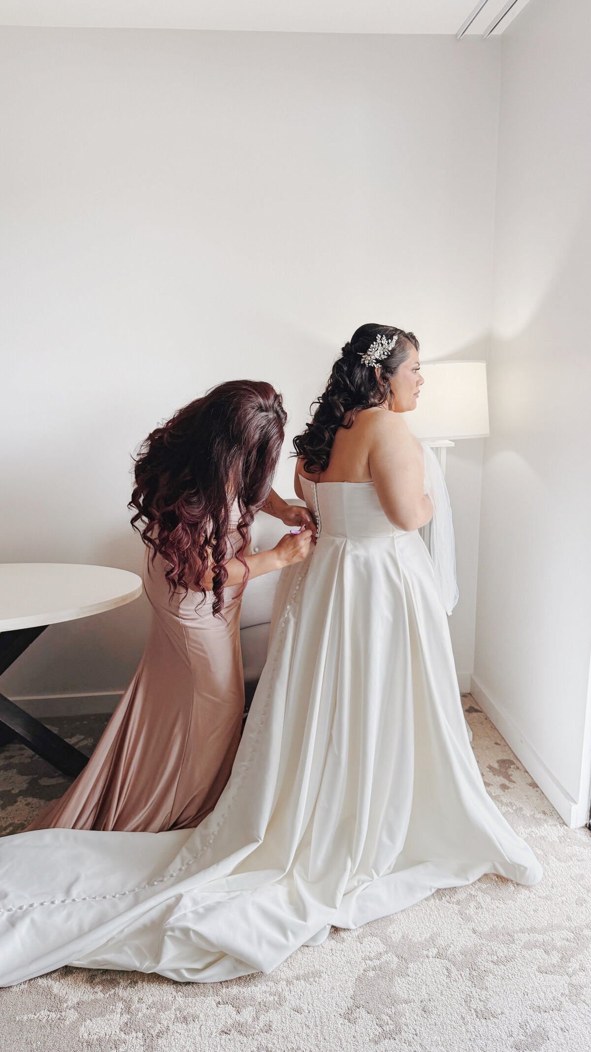 Bridesmaid helping bride zip up her dress at Lake San Marcos in California.