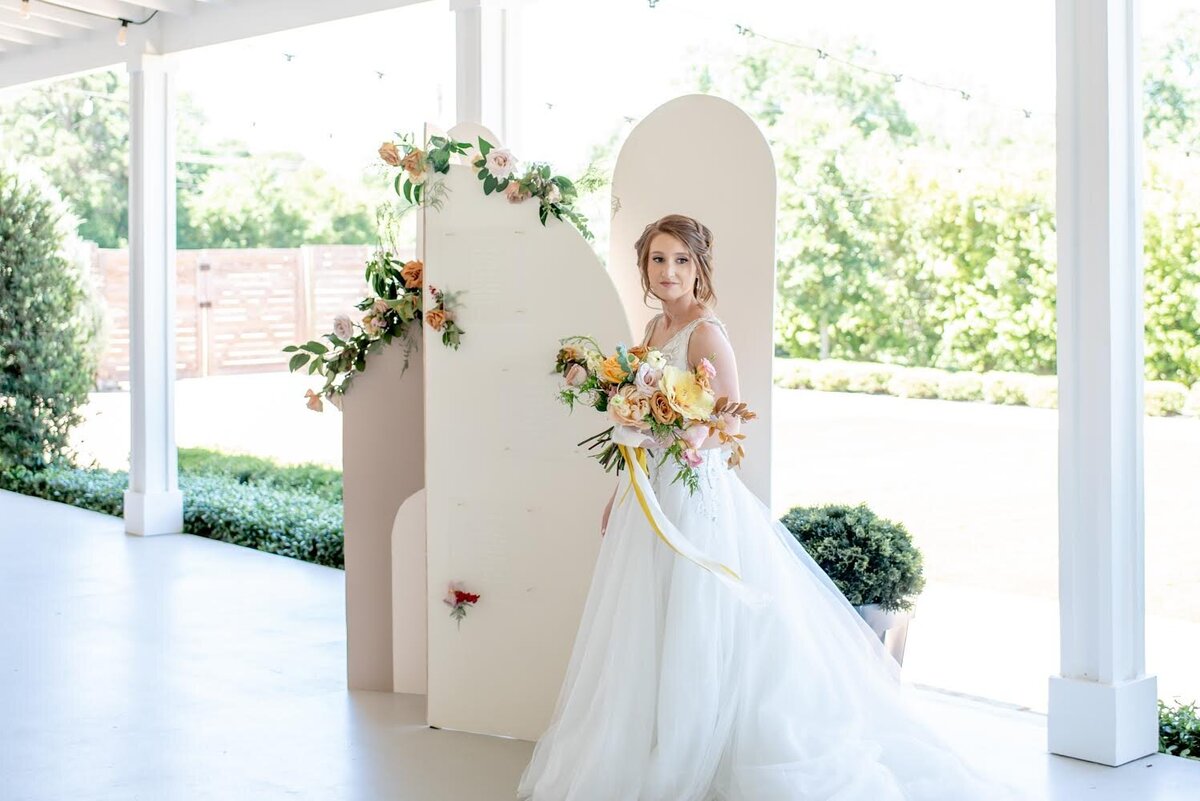Bride standing in front of a neutral colored arch backdrop on wedding day