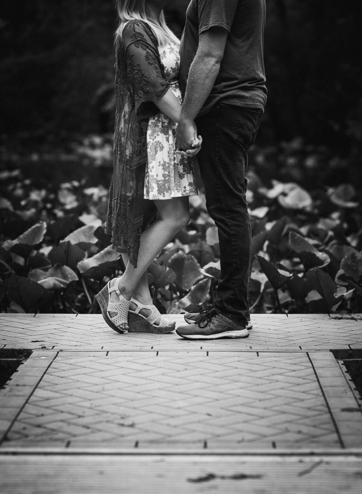 A black-and-white image of a couple holding hands, standing close on a pathway