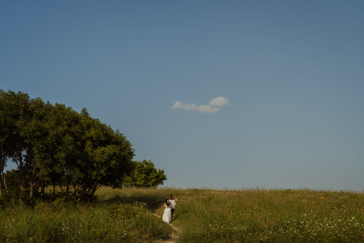 A dynamic, wide-angle capture of a couple walking across a grassy field, emphasizing their bond at White Rock Lake park.