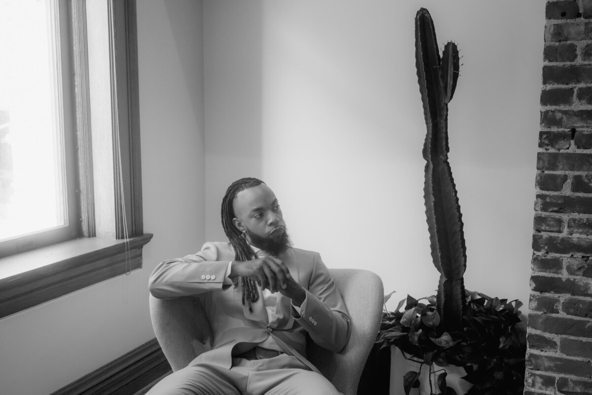 Man in a suit sitting on a chair besides a cactus.