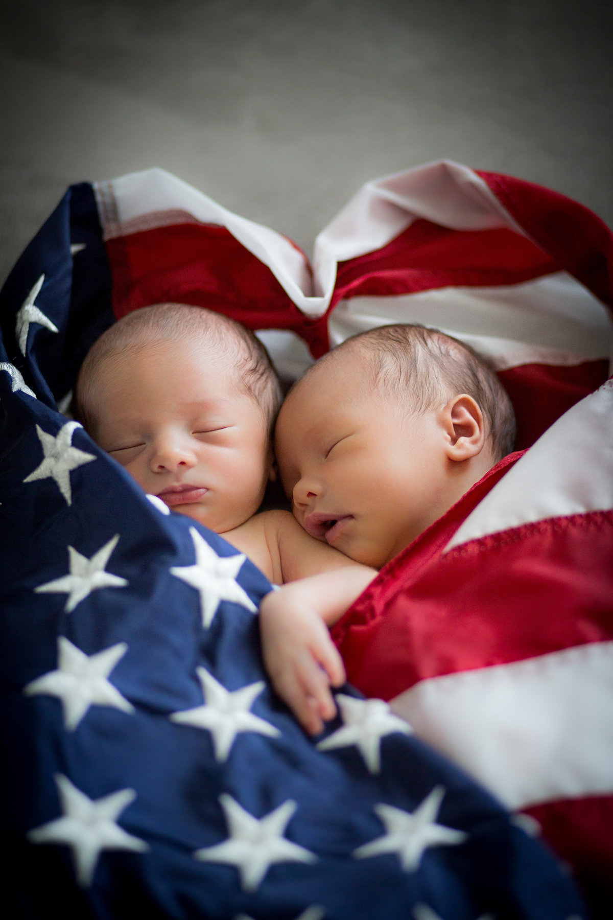 Newborn twins photography session of two infants wrapped in the American flag.