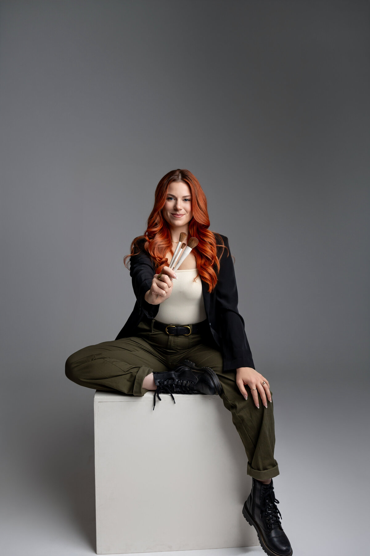 Woman with red hair sitting at table with confident expression in studio. Photograph by Yucaipa branding photographer Kaitlyn Dawn Photography.