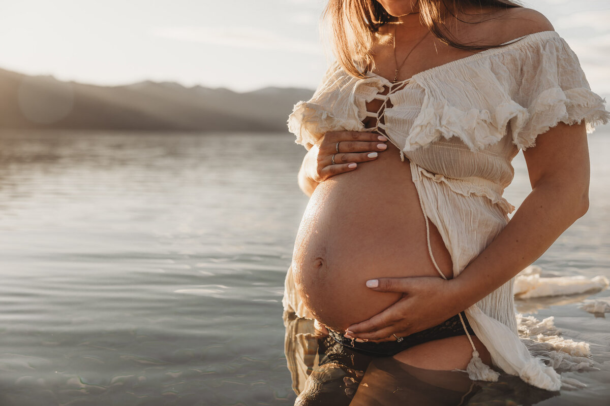 pregnant woman standing with hand on belly in the lake during her maternity session
