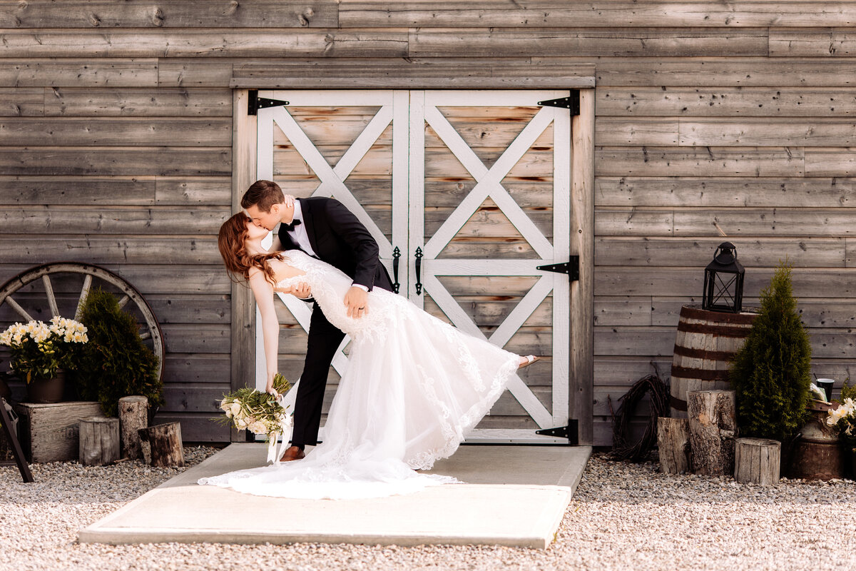 Groom dips and kisses bride in front of Willow Lane Barn