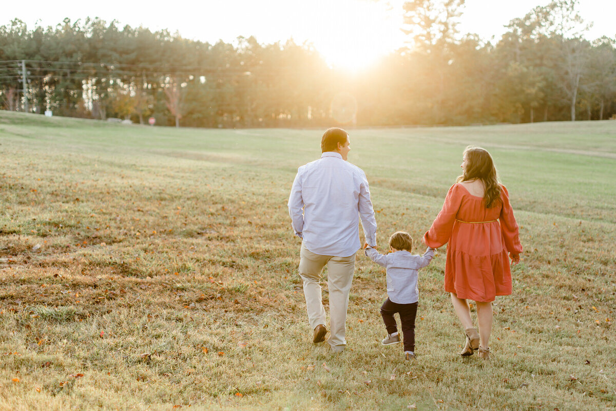 Family of 3 walk while holding hands towards a sunset in Flowery Branch