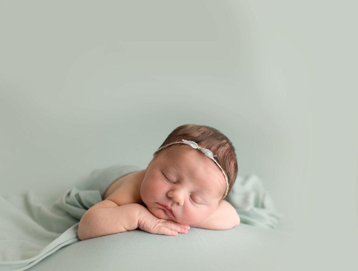 Baby girl on sage green backdrop with head on hands