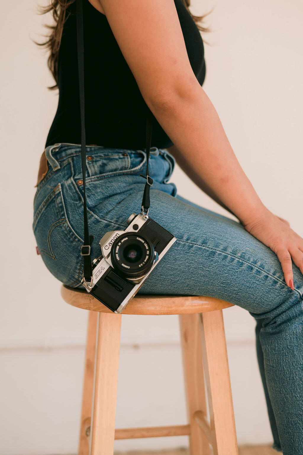 close up video of camera hanging off the shoulder of a woman sitting on a stool