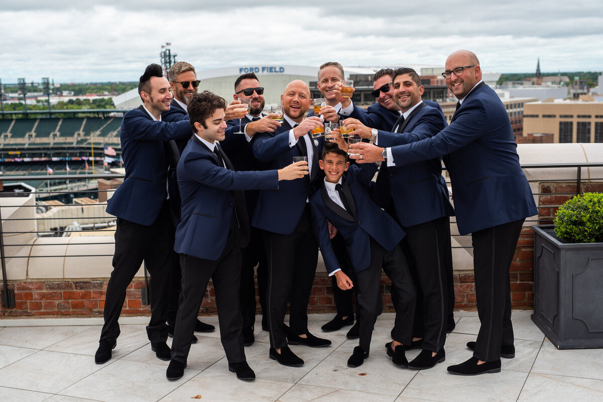 Groom and groomsmen cheering on the rooftop downtown Detroit before wedding ceremony.