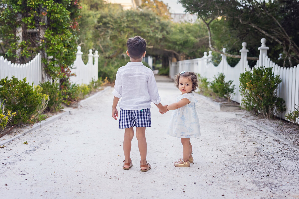 brother and sister walking on path with little toddler girl looking at camera at Seaside Florida.