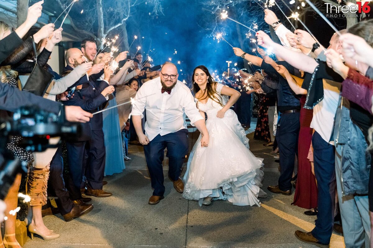 Bride and Groom run under a tunnel of sparklers held by wedding guests as they make a grand exit