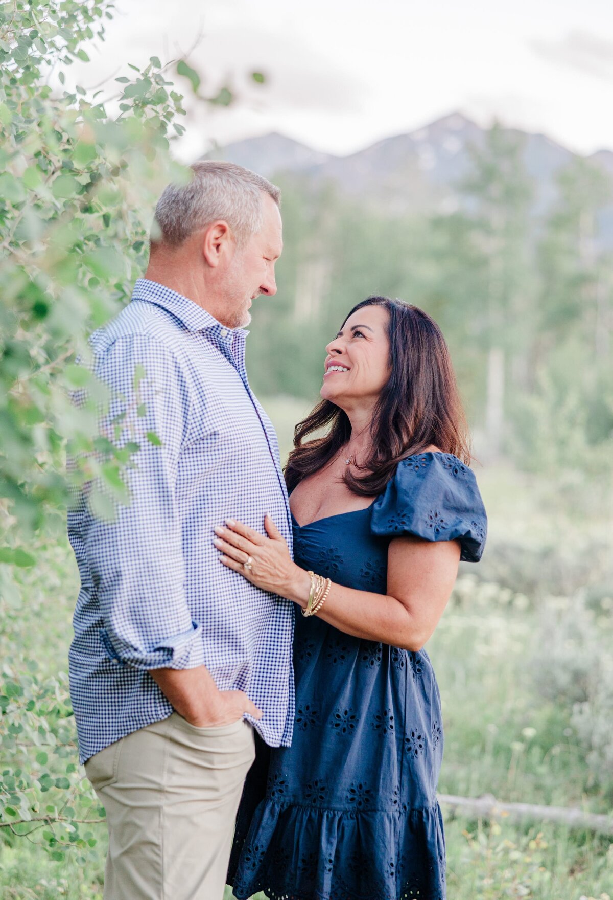 A man is hugged by his wife behind a tree in the mountains